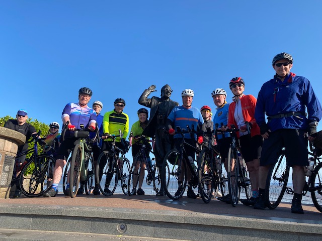An image of a group of cyclists next to a memorial.